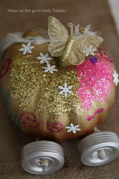 an apple painted with gold and pink glitter sitting on top of two white metal wheels