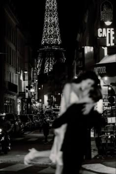 black and white photograph of people walking in front of the eiffel tower at night