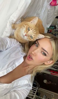 a woman laying on top of a bed next to an orange and white cat with blue eyes