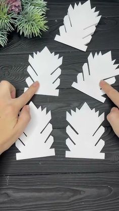 someone is cutting out paper leaves with scissors on a wooden table next to some succulents