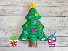 a crocheted christmas tree sitting next to presents on a white wooden background with wood planks