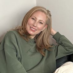 a woman sitting in a chair with her hand on her head and looking at the camera