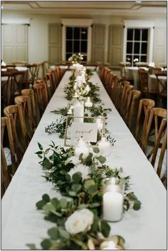 a long table with candles and greenery on it in a banquet hall or conference room