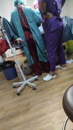 two people in scrub suits standing next to each other on a hard wood floor with chairs around them