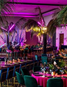 a room filled with lots of tables covered in purple and green cloths next to tall palm trees