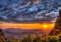 the sun is setting over some mountains and valleys in the distance, with trees on either side