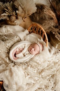 a newborn baby is wrapped in a white blanket and laying on a bed with feathers