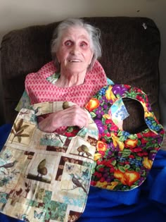 an older woman sitting on a couch holding two bibs