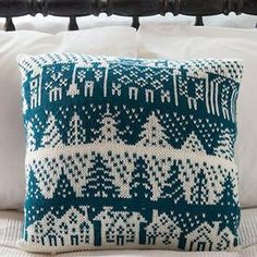 a blue and white knitted pillow sitting on top of a bed next to pillows