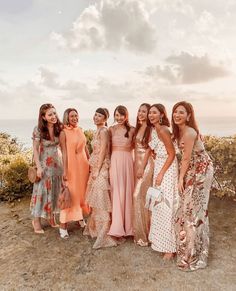 a group of women standing next to each other on top of a dirt field near the ocean