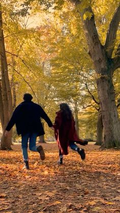 two people are running through the leaves in an open area with trees and yellow foliage