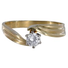 a gold ring with a white diamond on the center and two curved bands around it