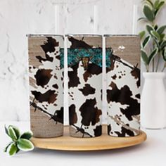 three cow print flasks sitting on top of a wooden tray next to a plant