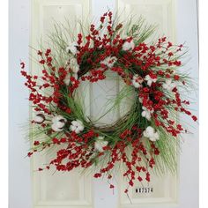 a wreath with red berries and white cotton is hung on the front door to welcome guests