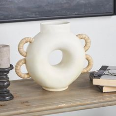 a white vase sitting on top of a wooden table next to a candle and books