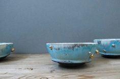 three blue bowls sitting on top of a wooden table next to each other with gold studded handles