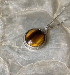 This petite pendant features a lovely, natural, Tiger's eye gemstone. I chose this gemstone because I have always been drawn to its energy! I loved the movement in the stone, and wanted to keep the setting simple but unique. I started with a pure silver, serrated, bezel wire, to secure the stone. Then I created a sterling silver platform to reveal the back of the stone, while securing it. Then, I placed a glitterwire halo around the stone, attaching it to the top of the stone. then, I placed a single, tiny, sterling silver granules at the very top of the stone. I use the same glitter wire to create a matching bale (4mm) allowing for a variety of chains to comfortably be threaded through! I love the final look, and feel that it is sleek and modern, the perfect addition to any wardrobe! I ha Natural Stones Birthstone Necklace With Round Pendant, Everyday Round Necklaces With Natural Stones, Sterling Silver Birthstone Necklace With Natural Stones, Sterling Silver Round Birthstone Necklace With Natural Stones, Sterling Silver Necklace With Natural Round Stones, Handmade Sterling Silver Birthstone Necklace, Spiritual Birthstone Necklace With Round Gemstone, Spiritual Necklaces With Round Natural Stones, Spiritual Round Birthstone Necklace