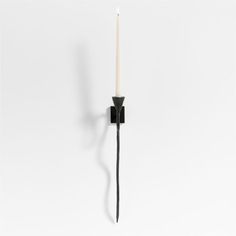 a black candle holder with a single white candle on the wall next to it, against a white background