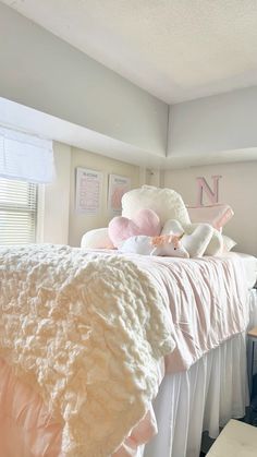 a bed with pink and white pillows on top of it in a bedroom next to a window