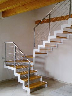 a white staircase with wooden handrails next to a wall and tiled flooring