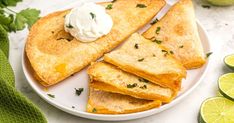 quesadillas on a plate with sour cream and limes next to them