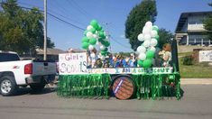 a parade float with balloons and streamers on the back in front of a white truck