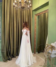 a woman standing in front of a chandelier wearing a wedding dress with long sleeves