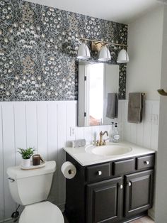 a white toilet sitting next to a sink in a bathroom under a mirror and lights