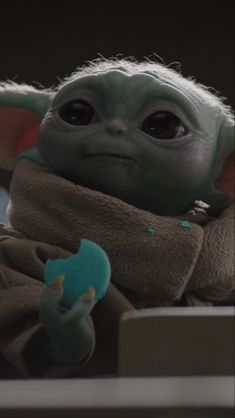 the child yoda is sitting down and holding a blue object in his hands,