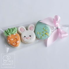 three decorated cookies in the shape of rabbits and carrots on a white surface with a pink ribbon