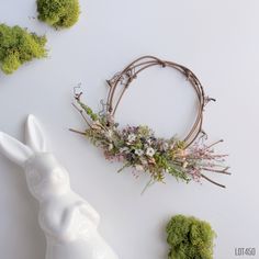 a white rabbit statue sitting next to a wreath with flowers and grass on it's head