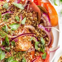 a white plate topped with sliced tomatoes and onions next to another plate filled with salad