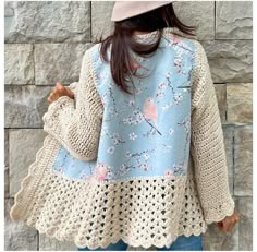 a woman standing in front of a stone wall wearing a blue sweater with pink birds on it