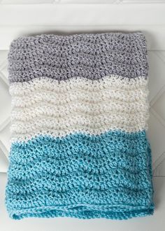 a crocheted blanket sitting on top of a white bed next to a pillow