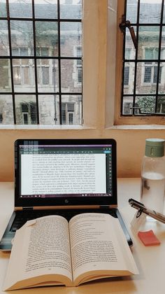 an open book sitting on top of a laptop computer next to a bottle of water