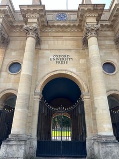 an entrance to the oxford university press building with columns and gates on either side, there is a clock in the top right corner