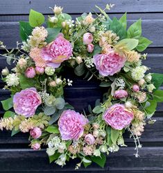 a wreath with pink flowers and green leaves on a black background is displayed in front of a wooden wall