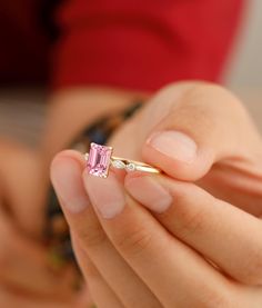 a person holding a ring with a pink stone in it's middle and one hand on the other side