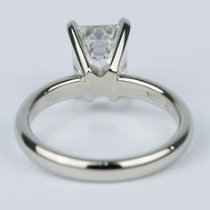 a white gold engagement ring with a princess cut diamond in the center, on a plain surface