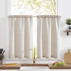 a kitchen window with white curtains and wooden cutting boards on the counter next to it