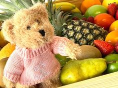 a teddy bear wearing a pink sweater next to a pile of fresh fruit and pineapples