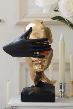 a gold and black statue with hands on it's face, next to white roses