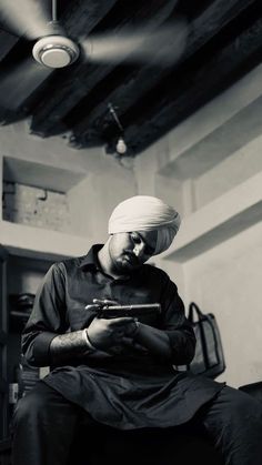 a man sitting in a chair looking at his cell phone while wearing a turban