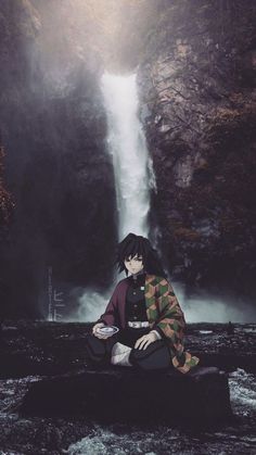 a man sitting on top of a rock next to a waterfall