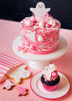 there is a pink cake with white decorations on the top and two cupcakes next to it