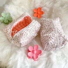 two small bags sitting on top of a white fur covered floor next to flowers and an orange flower