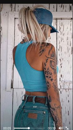 a woman with tattoos on her arms and back standing in front of a white wall