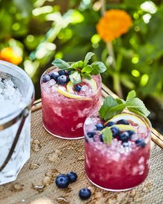 two glasses filled with blueberries and lemonade sitting on top of a wooden table