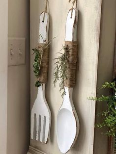 two white spoons hanging on a wall with twine and greenery attached to them