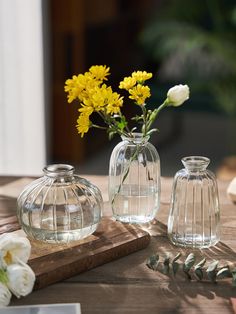 three clear vases with yellow flowers in them on a wooden table next to a book